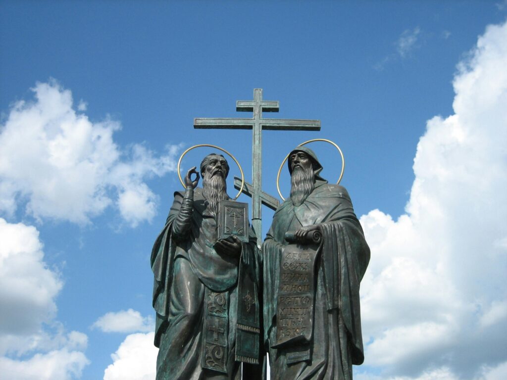 Bronze statues of saints with a cross under a clear blue sky.